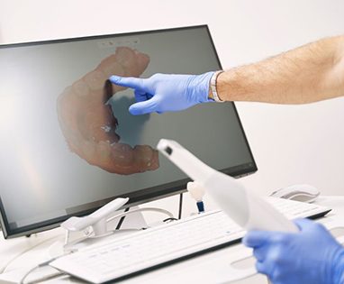 Dentist holding digital impression scanner and pointing at computer monitor